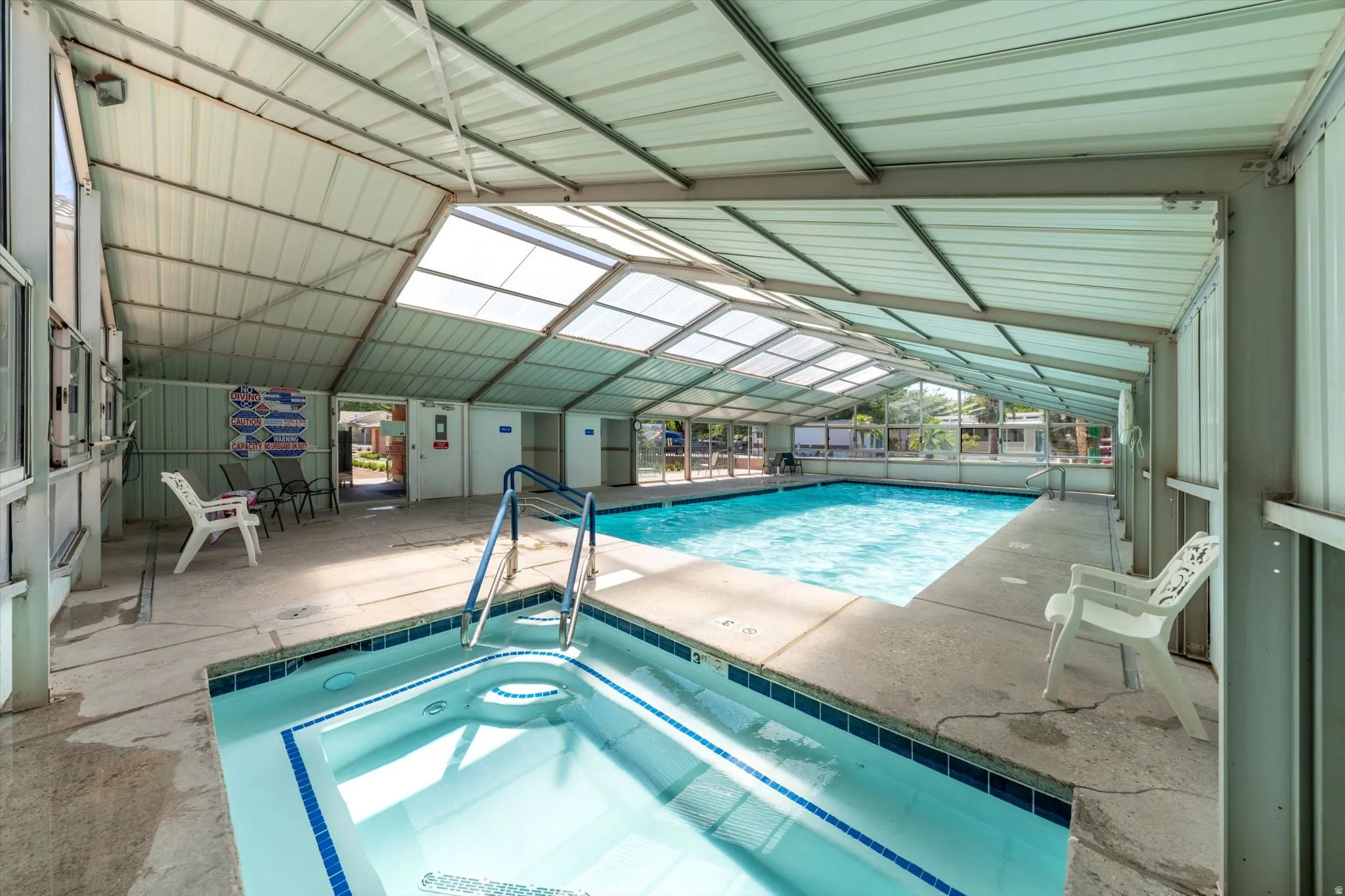 Enclosed indoor swimming pool with a connected spa, featuring a translucent roof and side panels