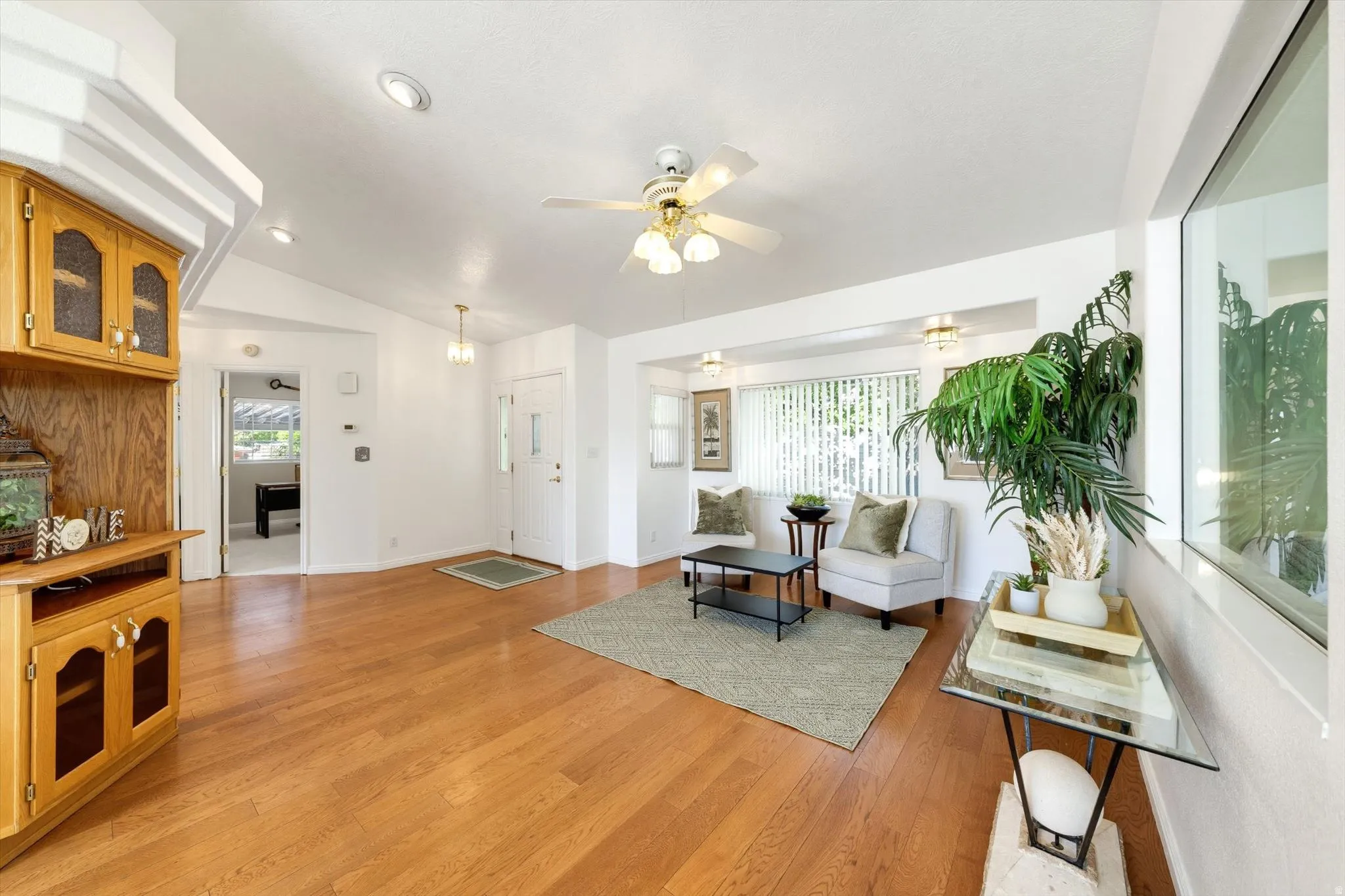 Wood-finish flooring, vaulted ceilings, recessed lighting, built-in cabinetry with glass panel doors, and a ceiling fan with integrated lighting