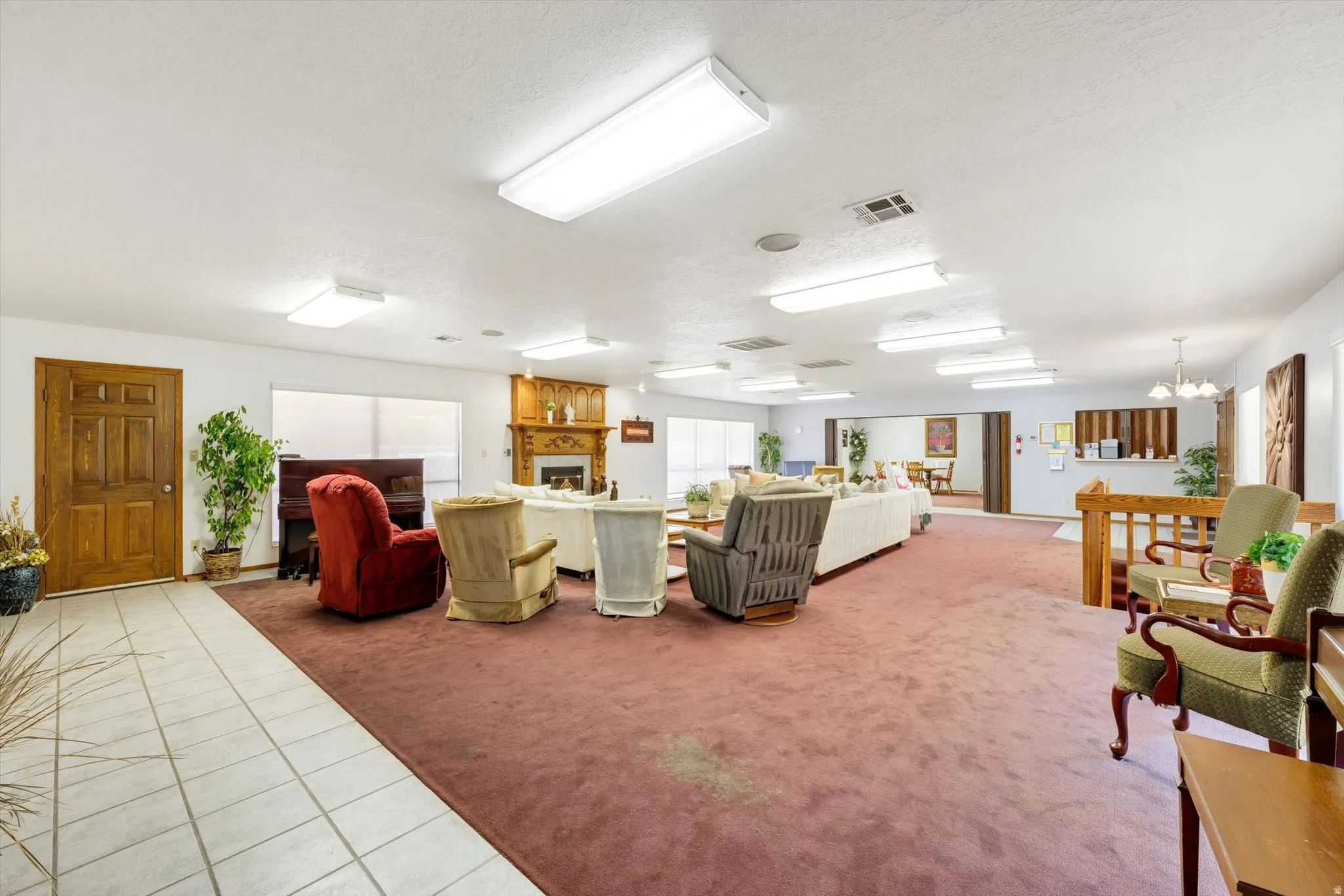 Spacious living area featuring extensive carpeting, a wood-finish entry door, and multiple ceiling-mounted light fixtures