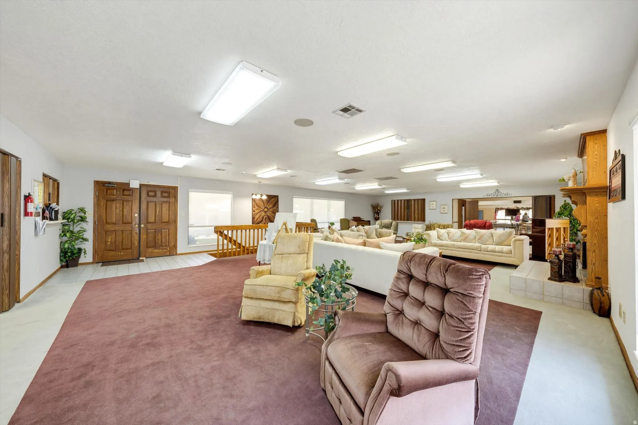 Expansive interior featuring twin wood-paneled entry doors, wood railing, recessed lighting, and a prominent built-in fireplace with a hearth