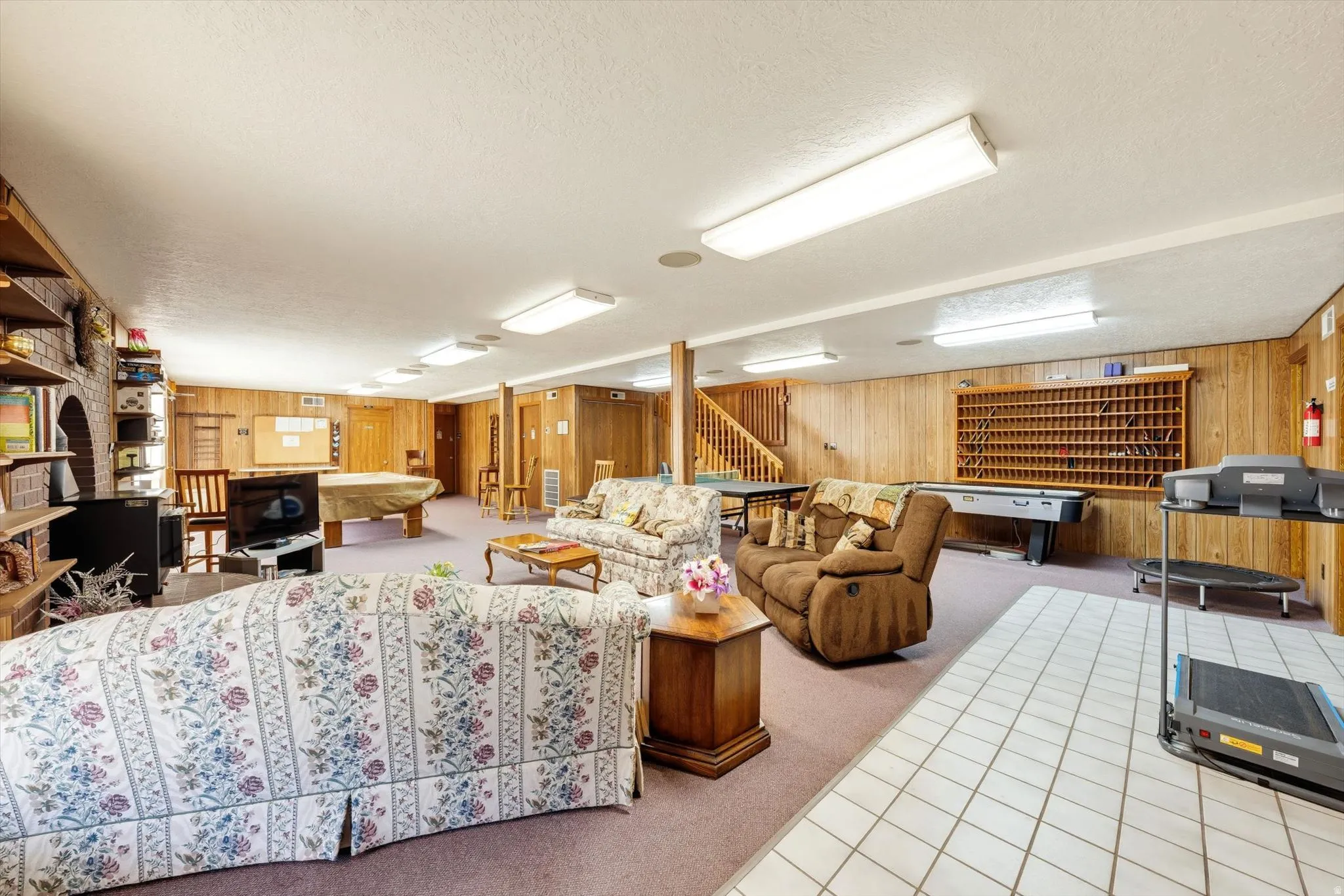 Spacious recreation room featuring wood paneling, carpeted flooring, and a built-in shelving unit