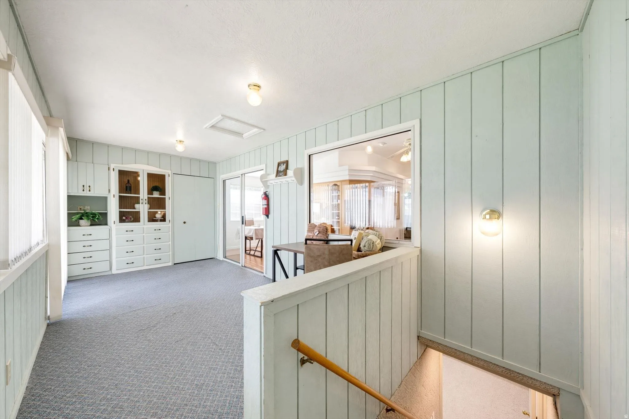 Built-in cabinetry with glass display doors, sliding glass door, overhead lighting, wall sconce, and wood-finish handrail