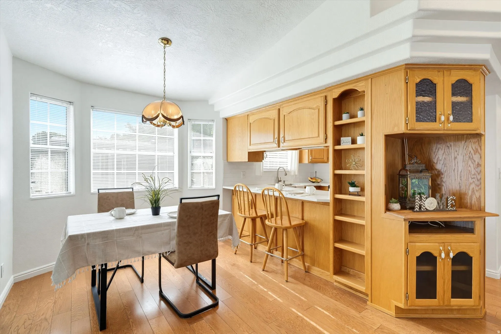 Hardwood-finish flooring, built-in wooden cabinetry, recessed shelving, and a bay window dining area with an attached pendant light fixture