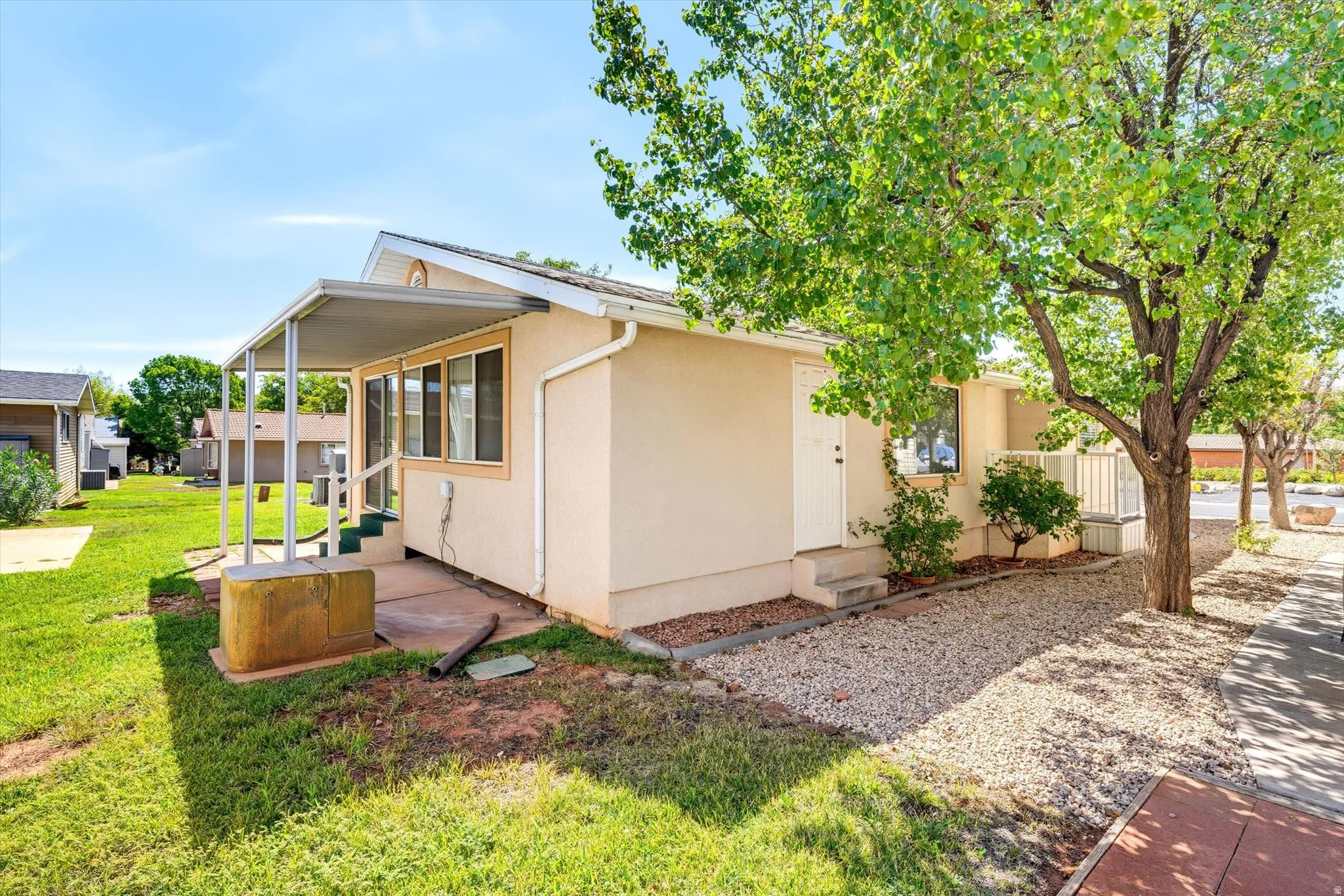 Exterior siding, covered patio, gravel landscaping, established trees, and a concrete walkway