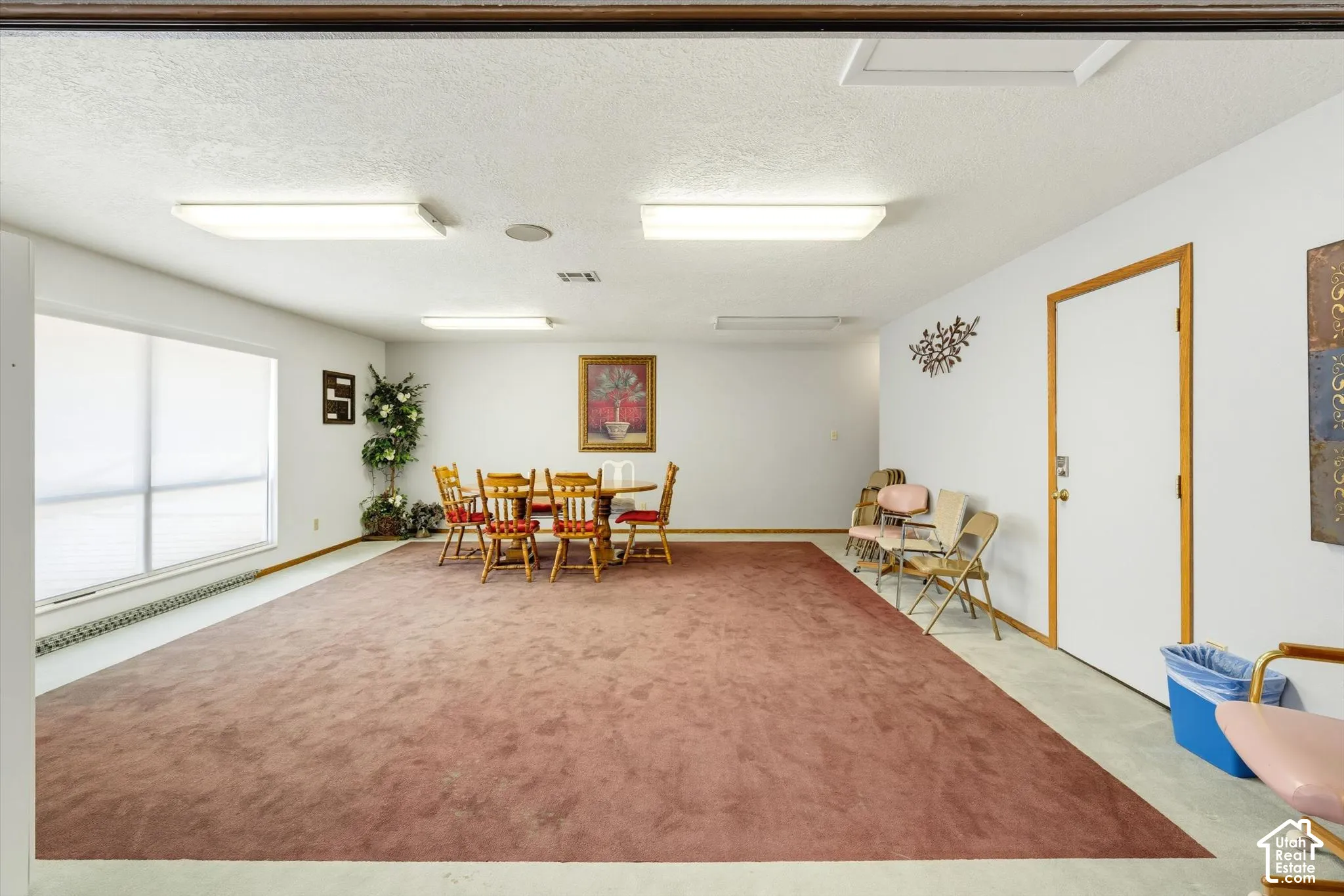 Spacious room featuring a wide window with roller shades, white walls, and a large area rug