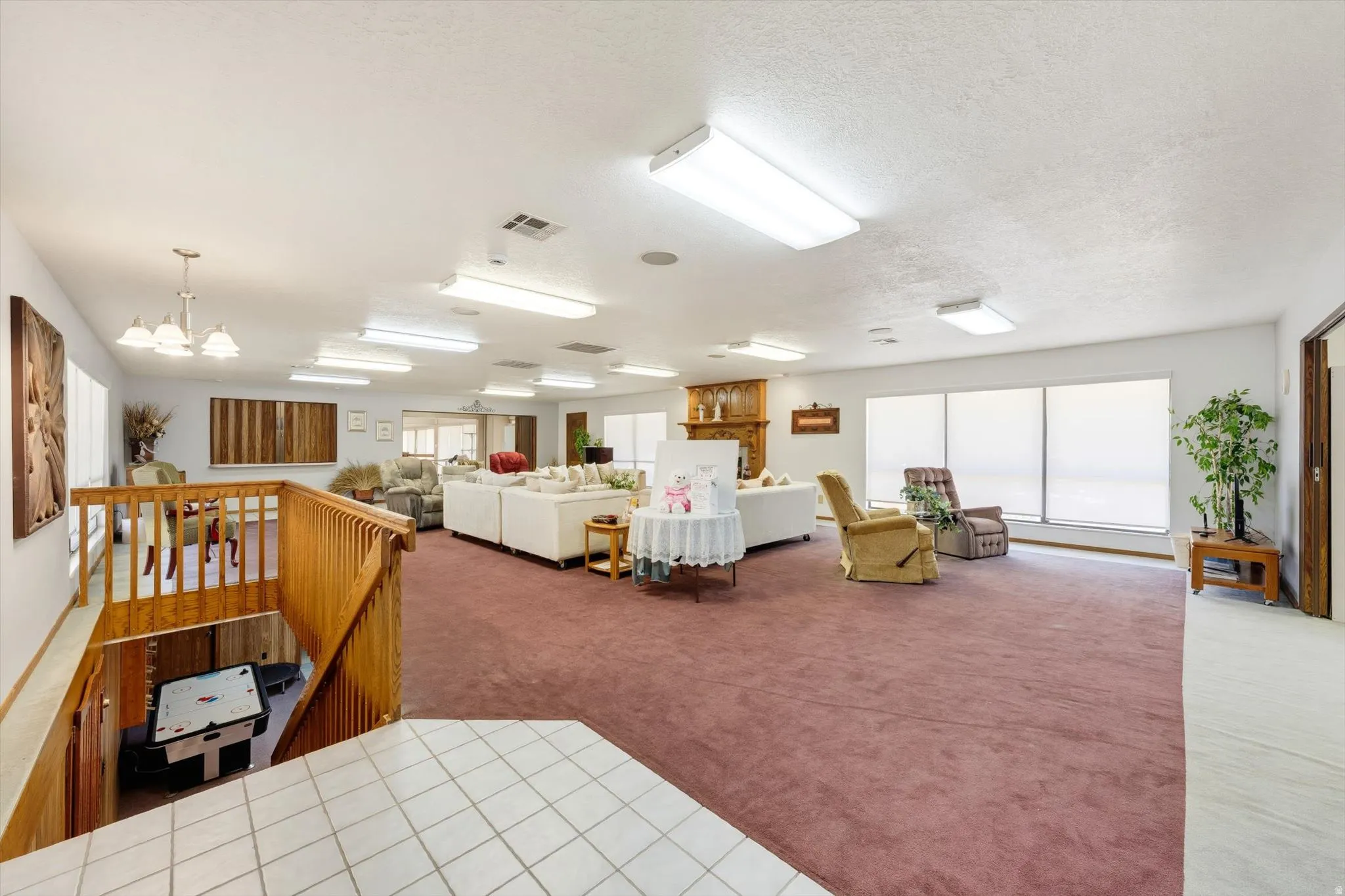 Expansive interior with carpeted flooring, multiple windows, a wood-finish staircase, and built-in overhead lighting