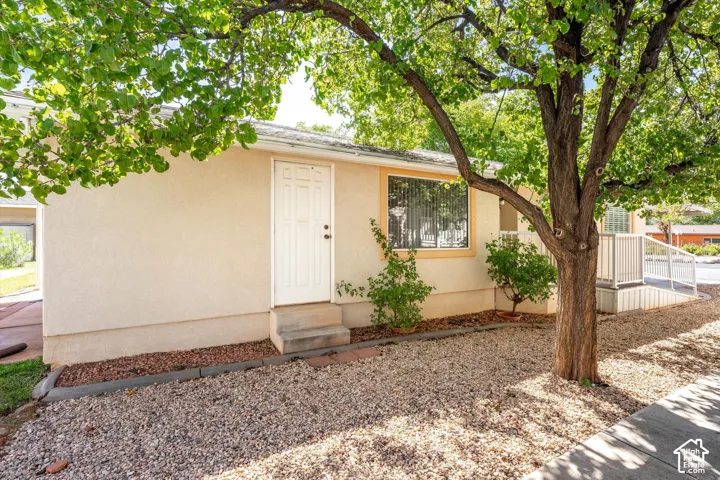 Stucco exterior with a security screen door, an accessible ramp, and a mature tree providing shade