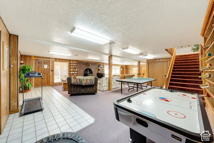 Expansive recreation room featuring wood-paneled walls, a brick fireplace, and a built-in shelving unit
