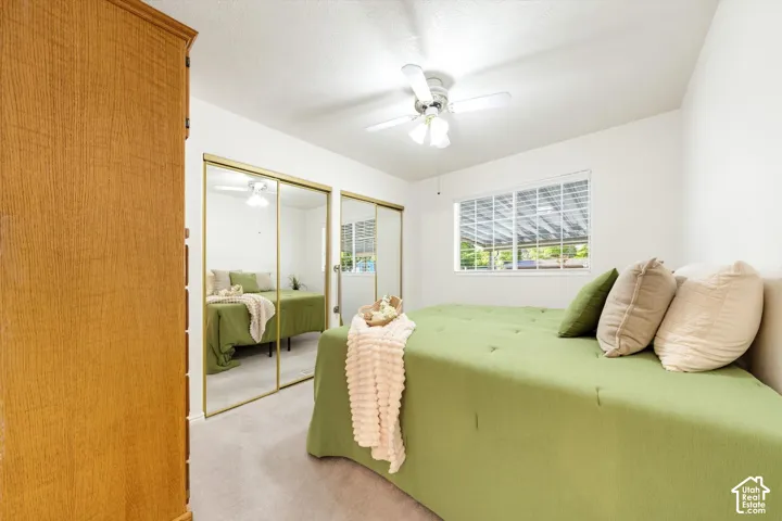 Integrated ceiling fan, neutral wall color, window with horizontal blinds, mirrored closet doors, and light-colored carpeting