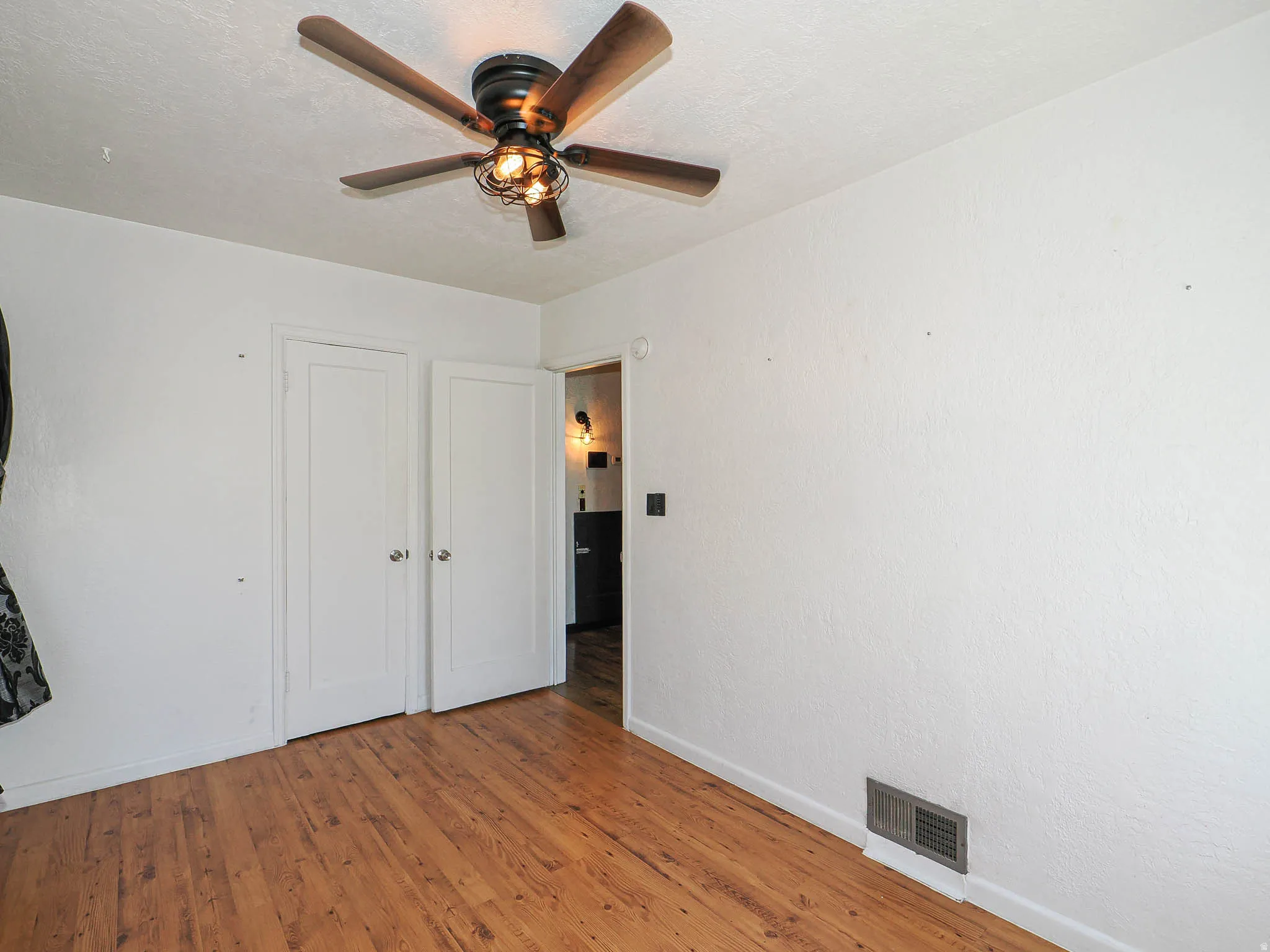 Second bedroom, wood-finish flooring, white painted walls, and a ceiling fan with light fixture