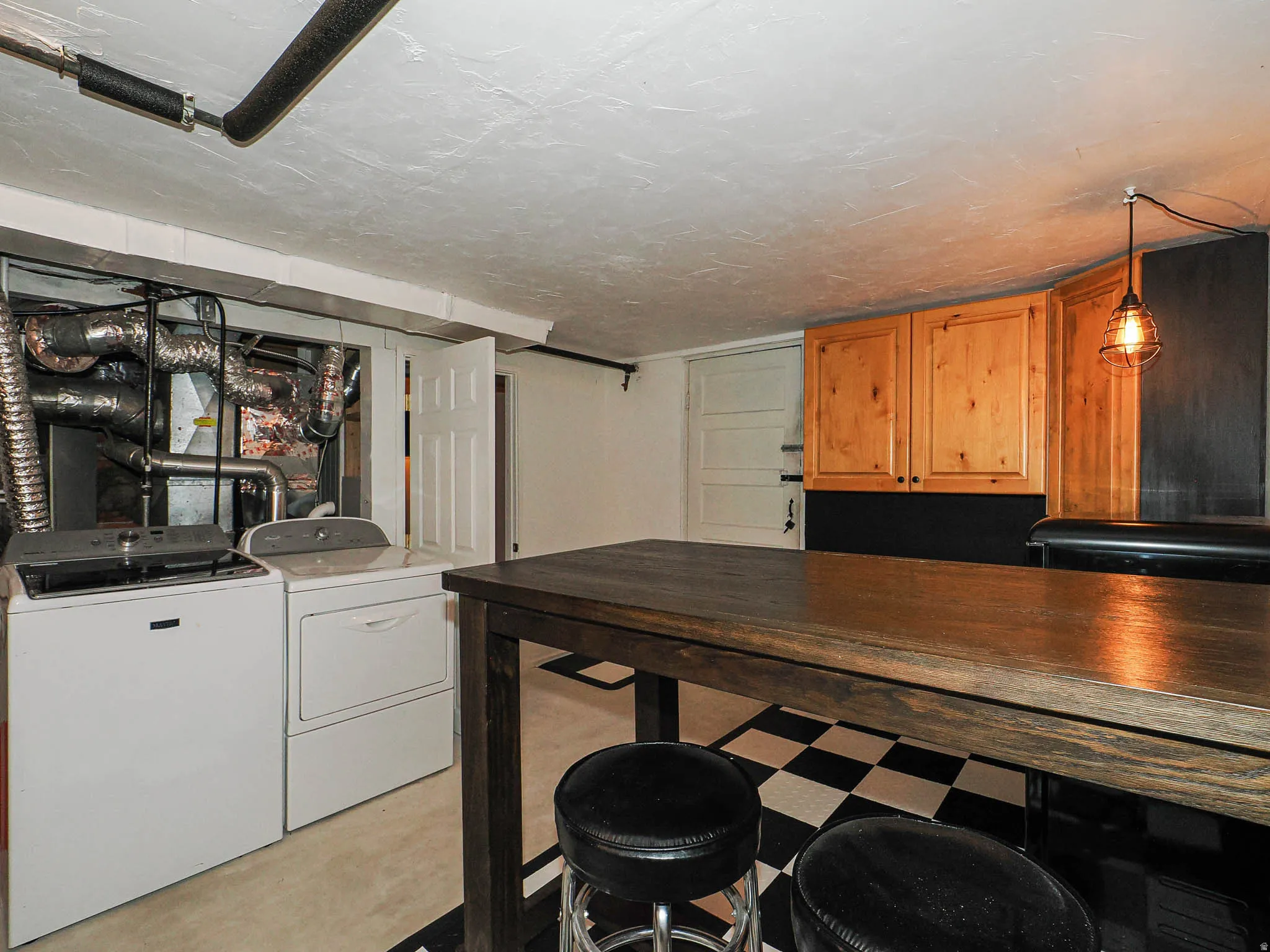 Finished basement space featuring a wood-finish bar, checkerboard flooring, upper wood-finish cabinetry,  industrial-style pendant lighting and door to garage.