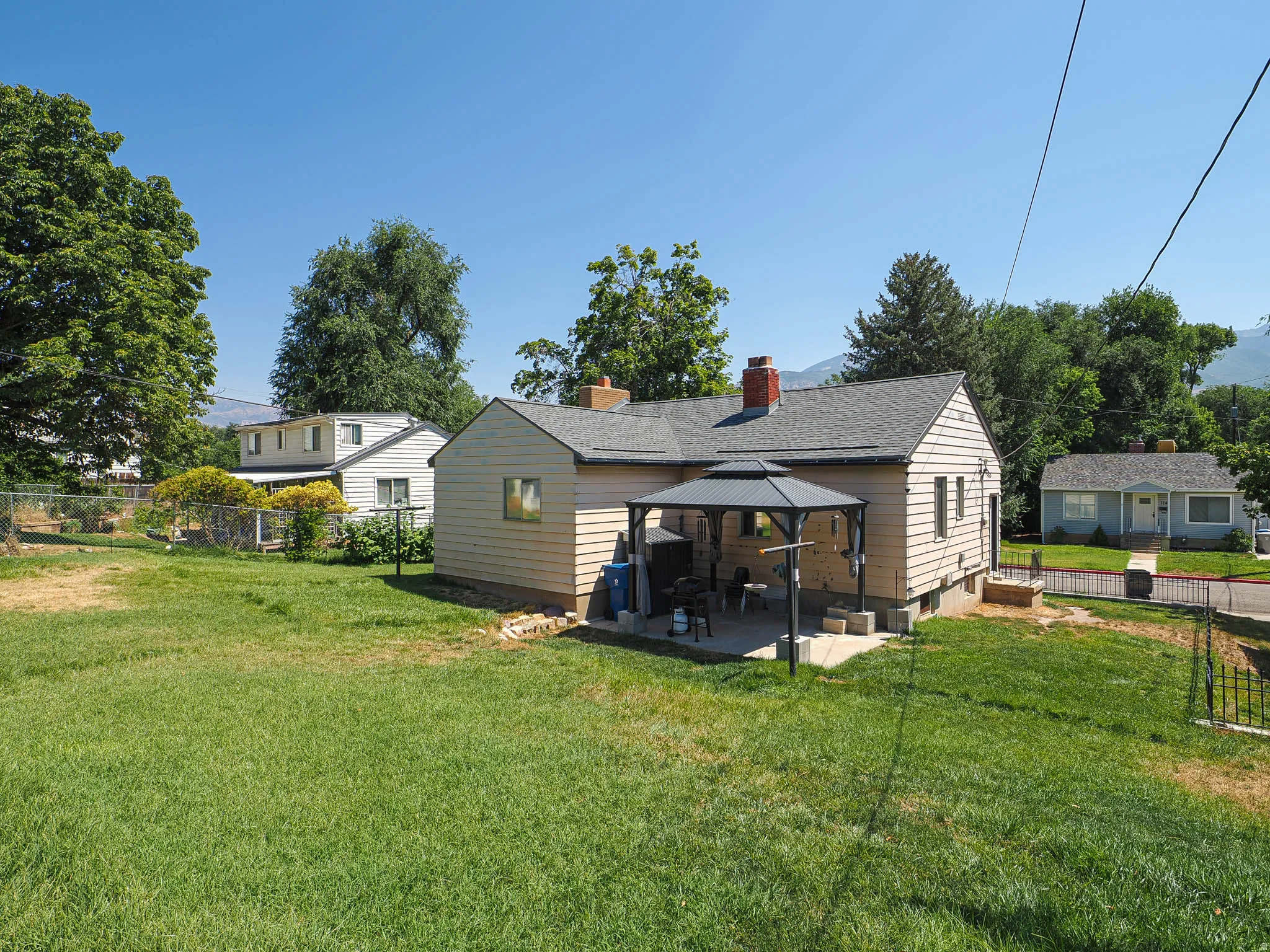 Spacious backyard featuring a large grass area, a concrete patio, and a covered gazebo