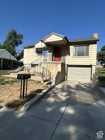 Split-level residence featuring a prominent red entry door, an attached garage, a concrete driveway, and a front entry porch with wrought iron railings