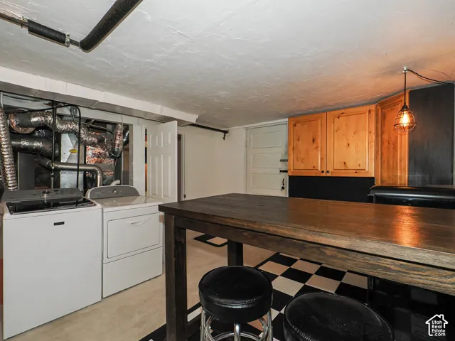 Finished basement space featuring a wood-finish bar, checkerboard flooring, upper wood-finish cabinetry,  industrial-style pendant lighting and door to garage.