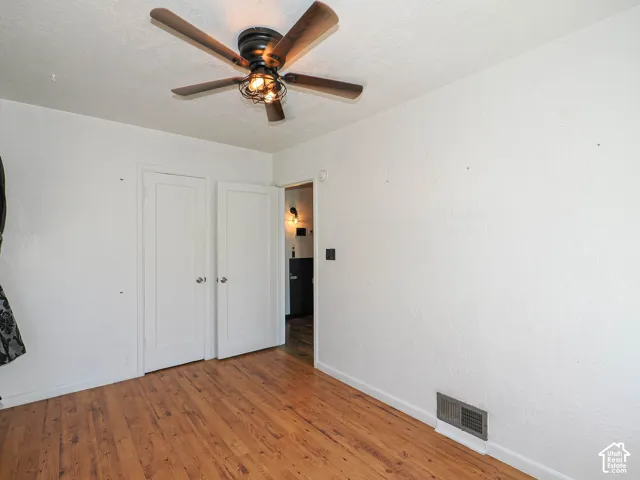 Second bedroom, wood-finish flooring, white painted walls, and a ceiling fan with light fixture