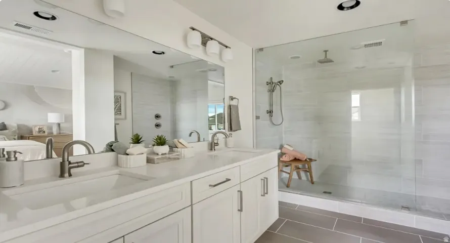 Contemporary bathroom featuring a double vanity with white cabinetry and integrated sinks, brushed nickel faucets, and an expansive glass-enclosed shower with a rain shower head and handheld spray. Home is TO BE BUILT. Pictures are of a similar model.