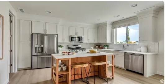 Kitchen featuring white cabinetry, stainless steel appliances, a center island with a light wood base, a white countertop, and wood-finish flooring. Home is TO BE BUILT. Pictures are of a similar model.