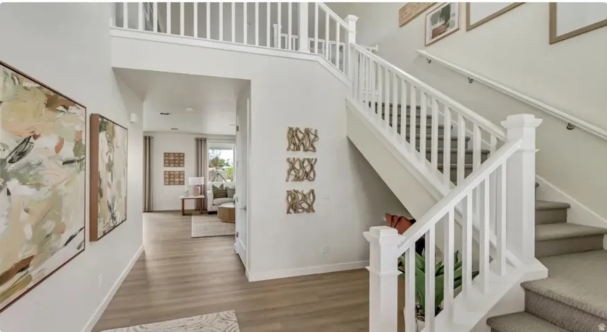 Two-story foyer featuring wood-finish flooring and a carpeted staircase with white balusters. Home is TO BE BUILT. Pictures are of a similar model.