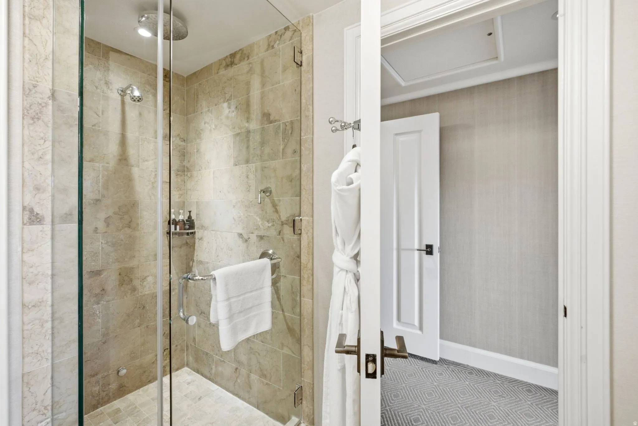 Walk-in shower featuring full-height stone tile, a rainfall shower head, and a separate handheld shower fixture