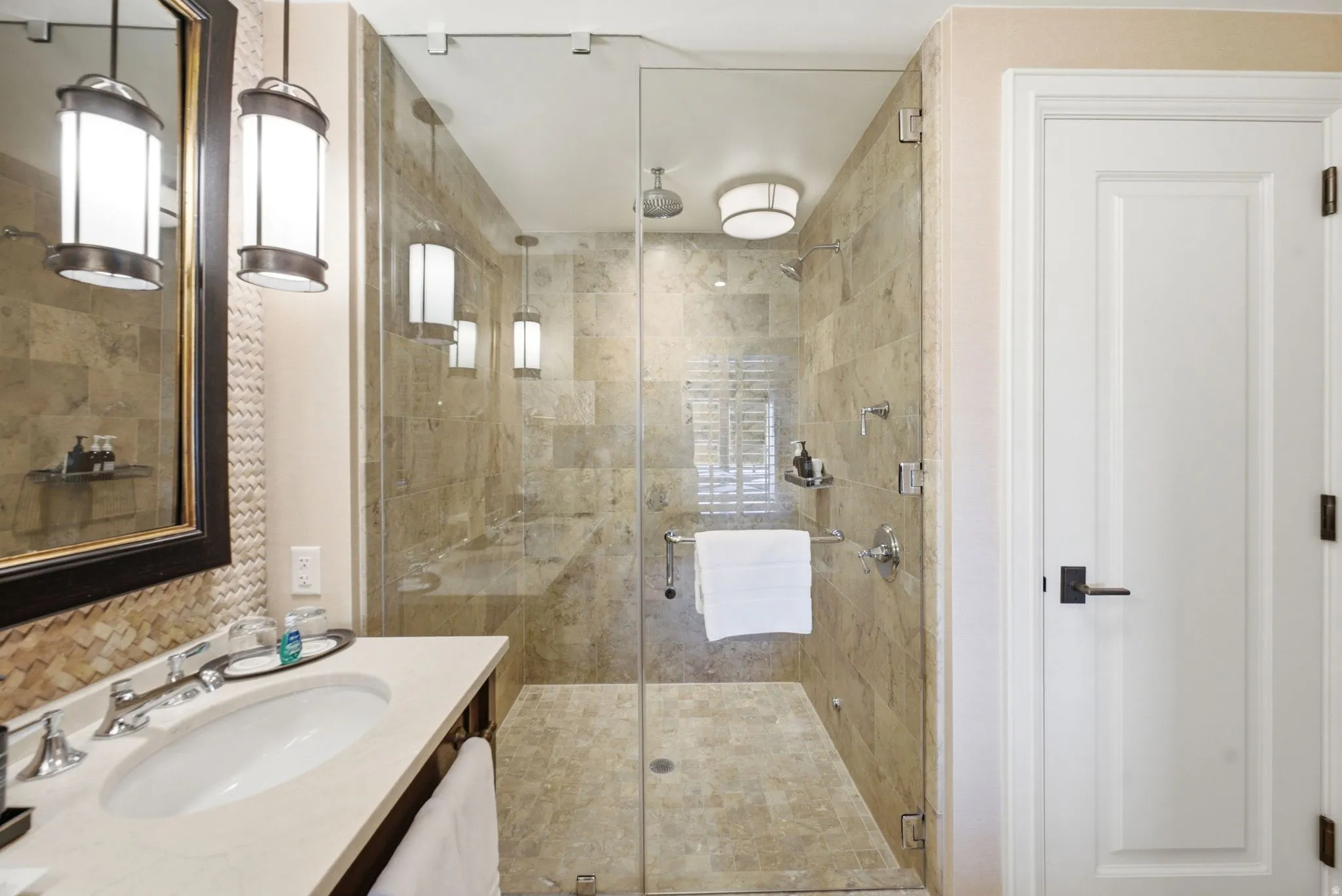 Full-glass shower enclosure with natural stone tile surrounds and a built-in bench