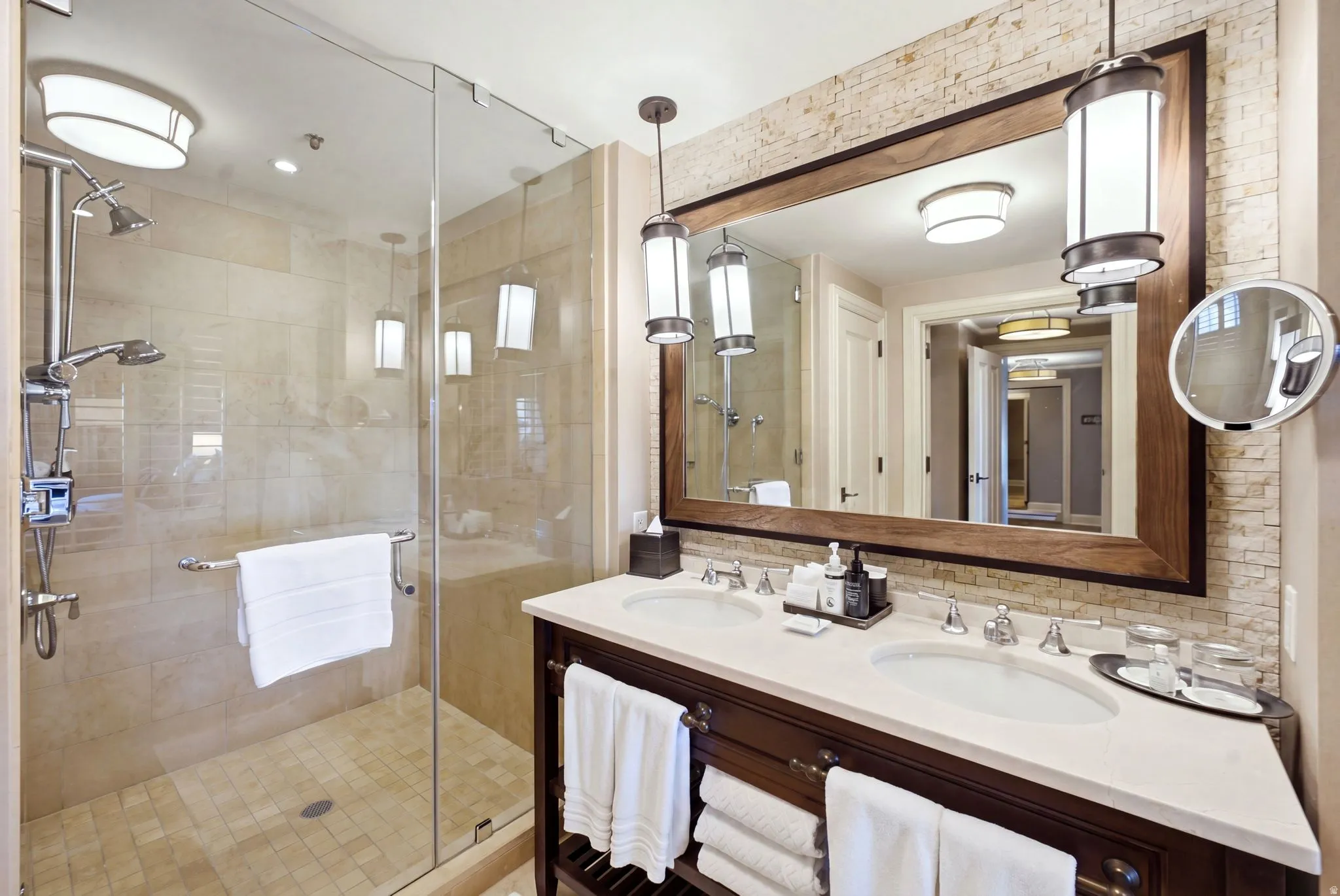 Bathroom featuring a glass-enclosed shower with dual shower heads, a double vanity with two undermount sinks, and a large framed mirror