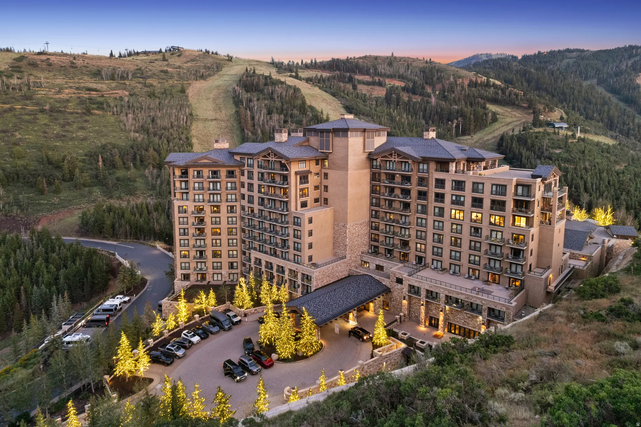 Multi-story resort-style building with stone and stucco exterior, featuring multiple balconies, a covered entryway, and a paved parking area