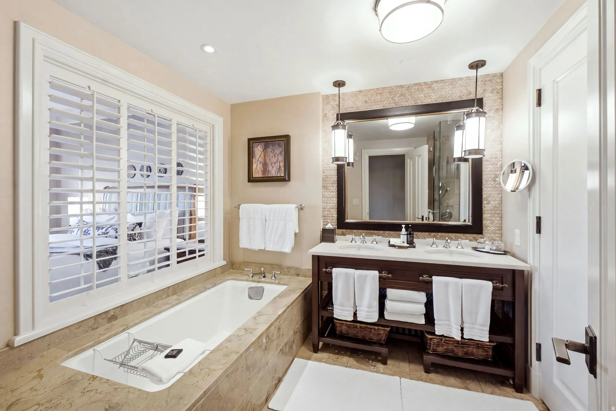 Soaking tub with stone surround, complemented by a dual vanity with a white countertop and dark wood cabinetry