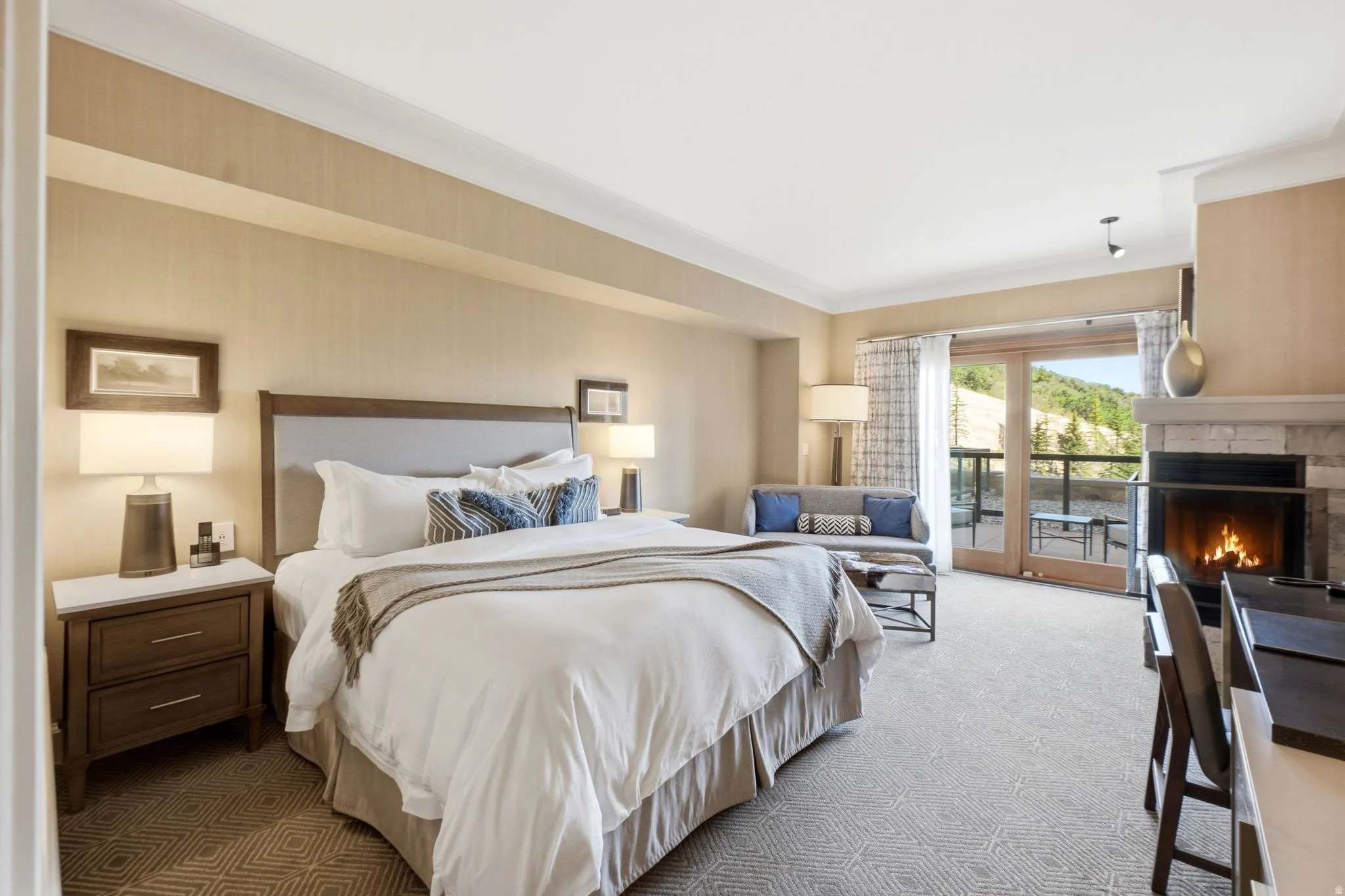 Spacious room featuring a stone fireplace, wood-finish French doors opening to an exterior balcony, and light-toned patterned carpeting
