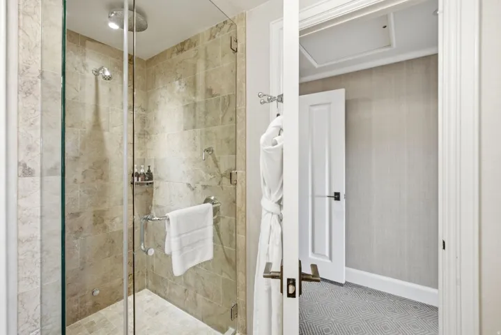 Walk-in shower featuring full-height stone tile, a rainfall shower head, and a separate handheld shower fixture