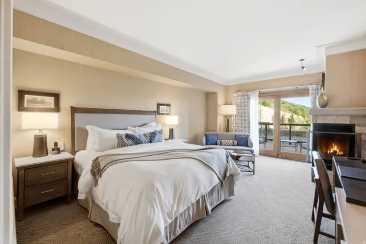 Spacious room featuring a stone fireplace, wood-finish French doors opening to an exterior balcony, and light-toned patterned carpeting
