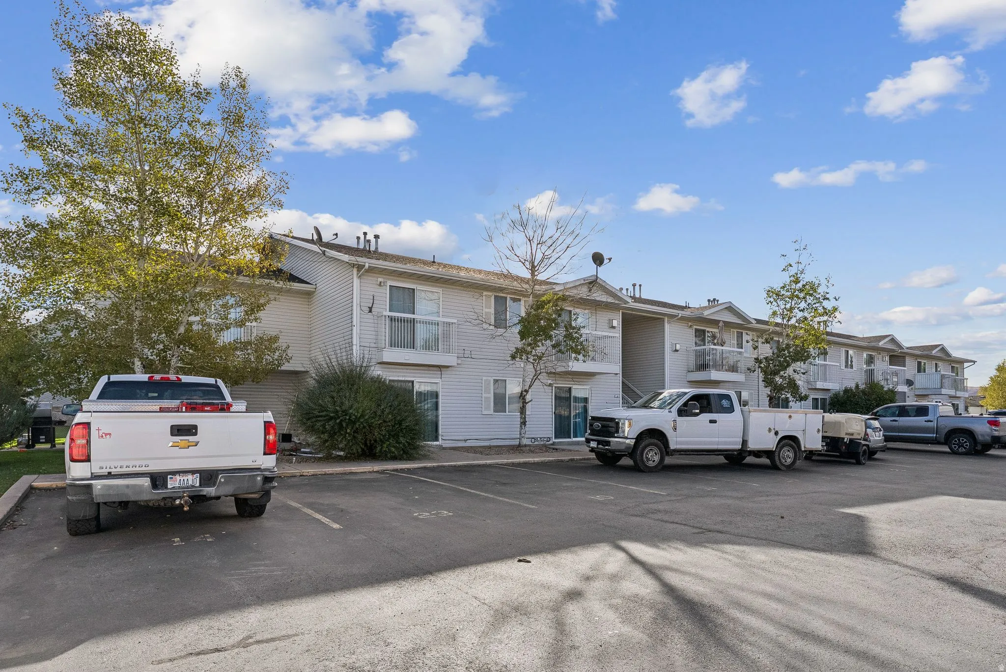 Multi-unit residential building featuring light-colored siding, multiple balconies with white railings, and sliding glass doors