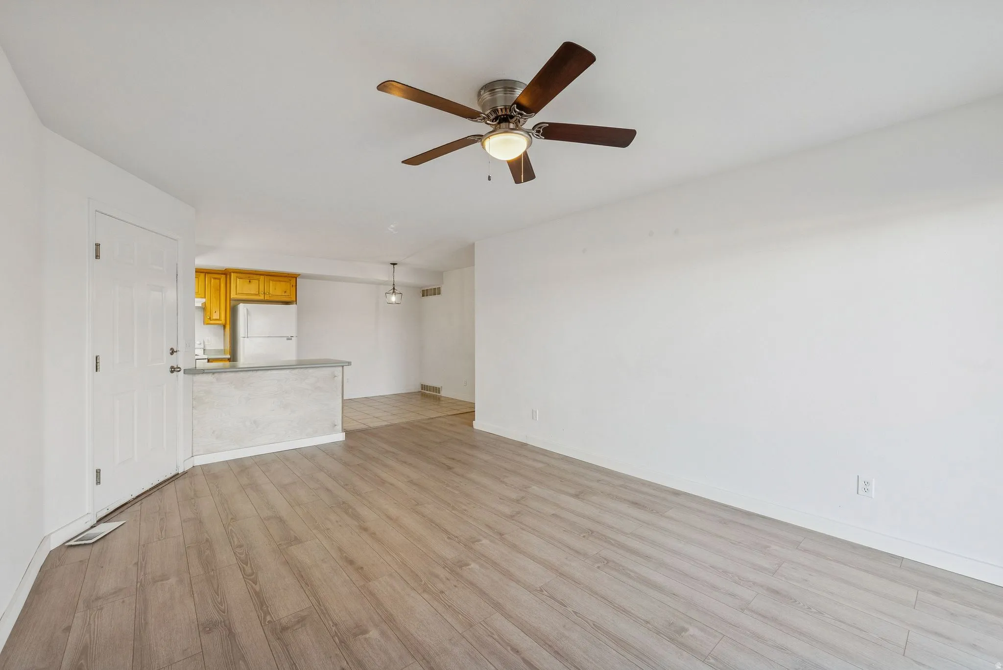 Open-concept living area featuring wood-finish flooring, a ceiling fan with integrated lighting, and a light-toned interior paint palette