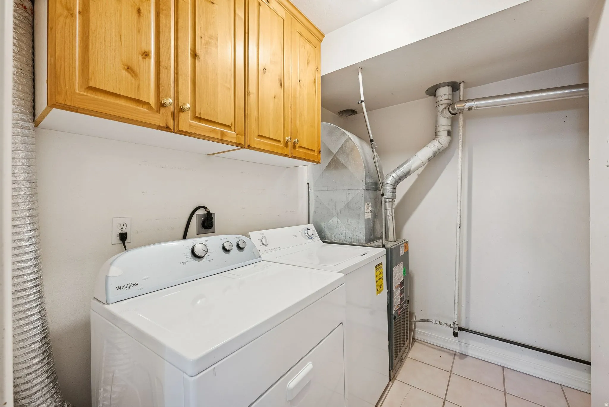 Laundry area featuring light wood-finish cabinetry, a white washer and dryer, and ceramic tile flooring