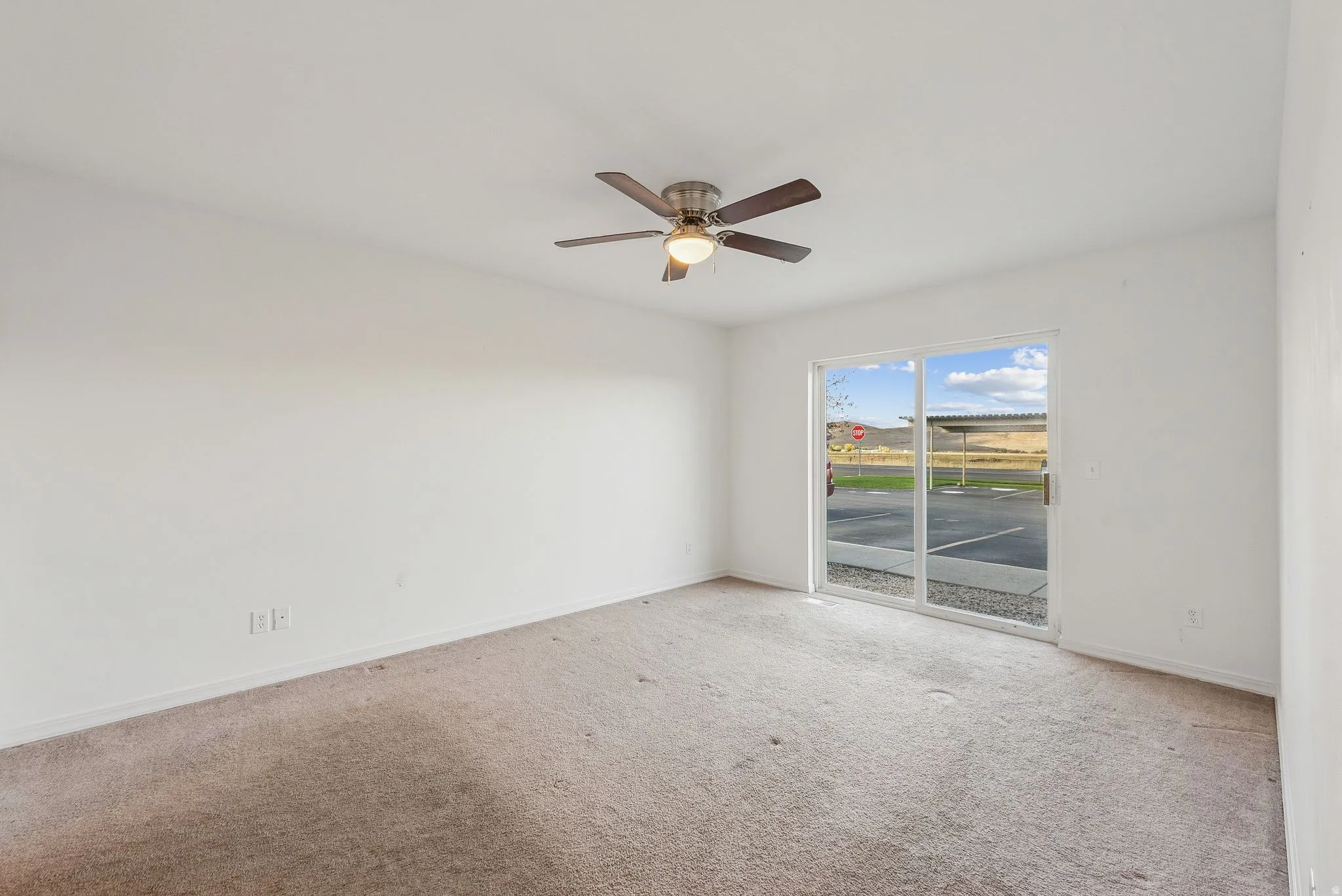 Spacious room featuring a ceiling fan with integrated lighting, white walls, and a sliding glass door providing external access