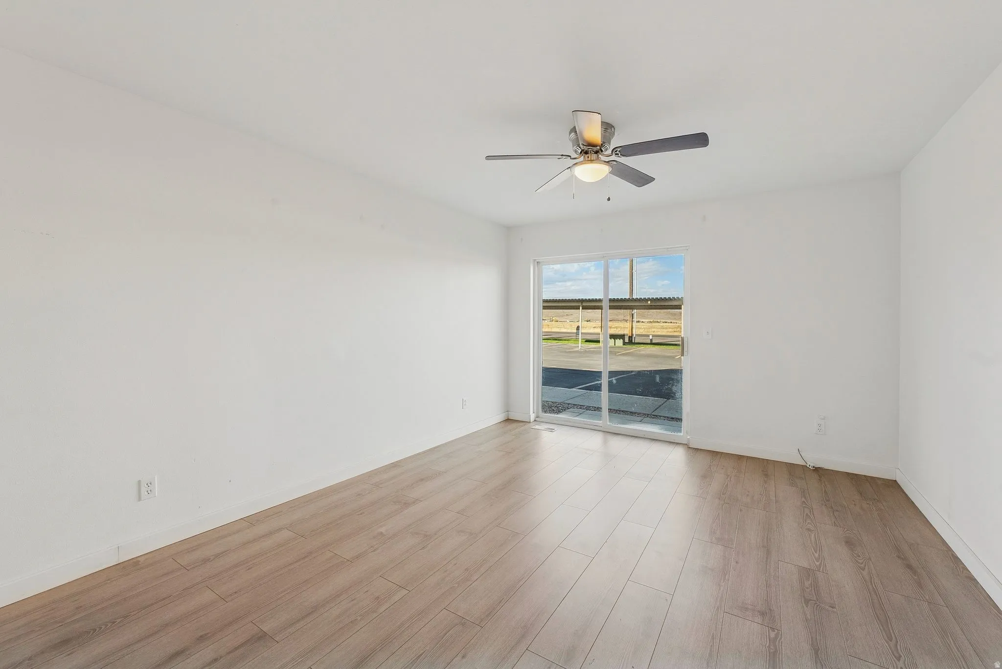 Spacious room featuring wood-finish flooring, white walls, and a ceiling fan with integrated lighting