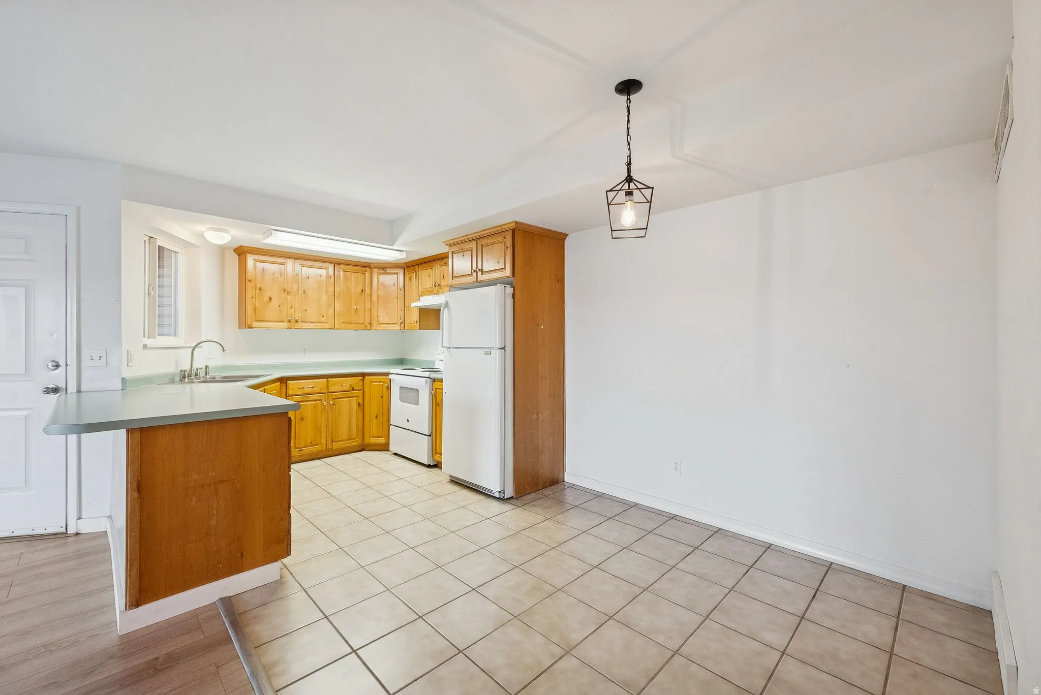 Kitchen and dining area featuring light wood cabinetry, white appliances, a peninsula with a countertop, tile flooring, and a contemporary hanging light fixture