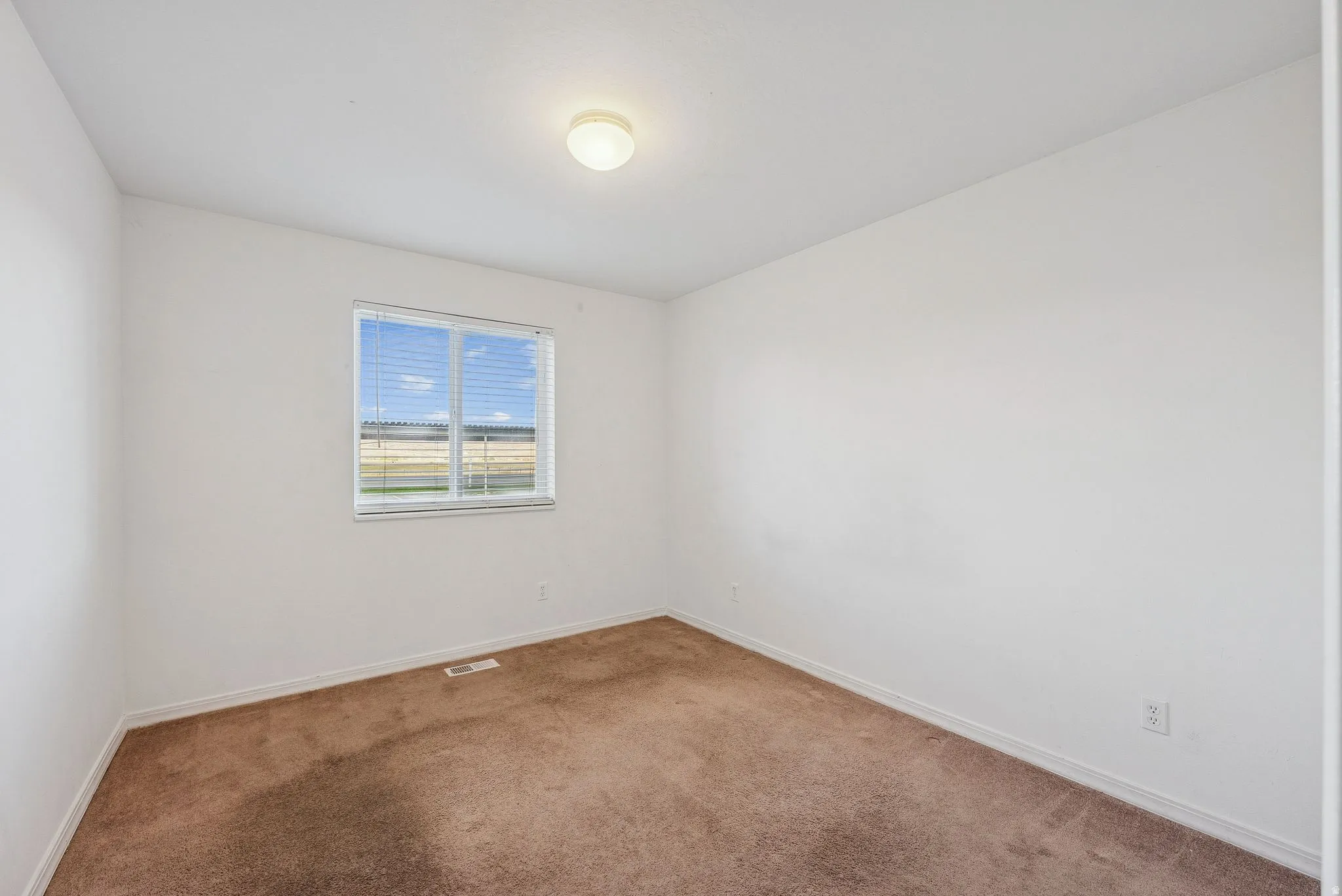 Carpeted room featuring a single window with horizontal blinds, a ceiling-mounted light fixture, and white painted walls