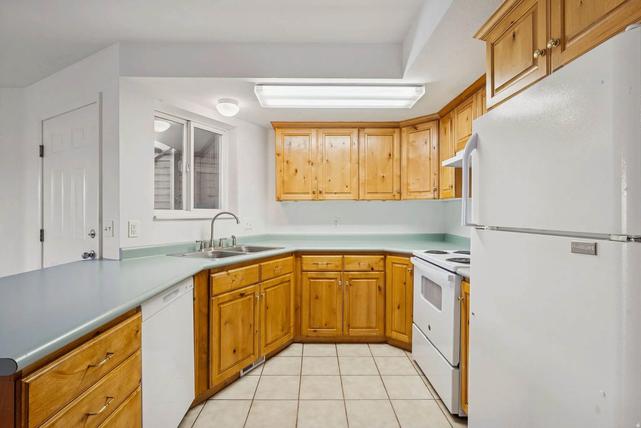Kitchen featuring wood cabinetry, light-colored countertops, white appliances, and tile flooring