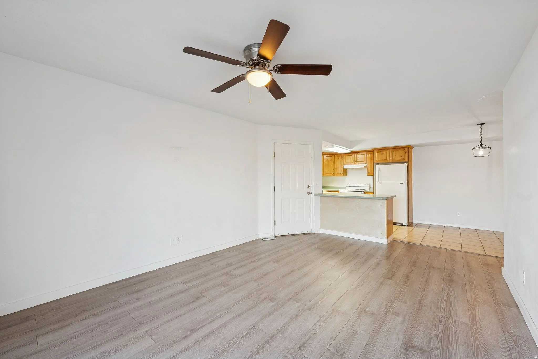 Spacious living area featuring wood-finish flooring, a ceiling fan, and white walls