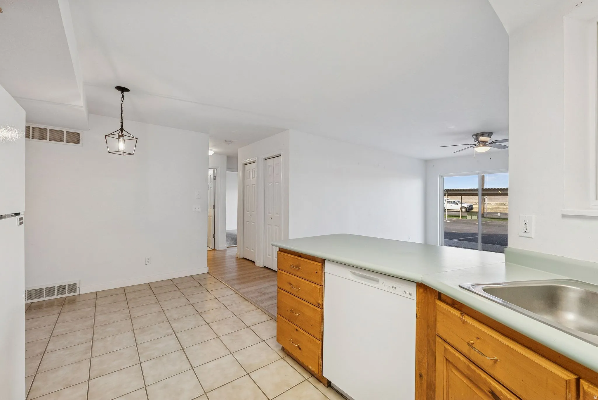 Kitchen area featuring light wood cabinetry, a built-in dishwasher, and a stainless steel sink with a light-colored countertop