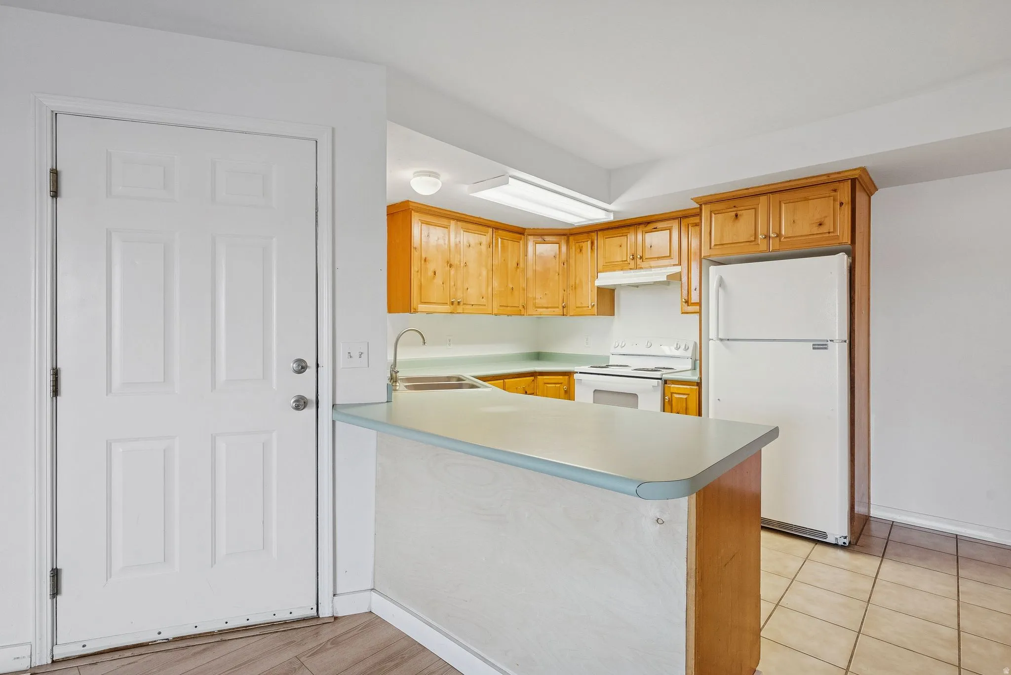 Kitchen featuring wood cabinetry, white appliances, light-toned countertops, and a breakfast bar