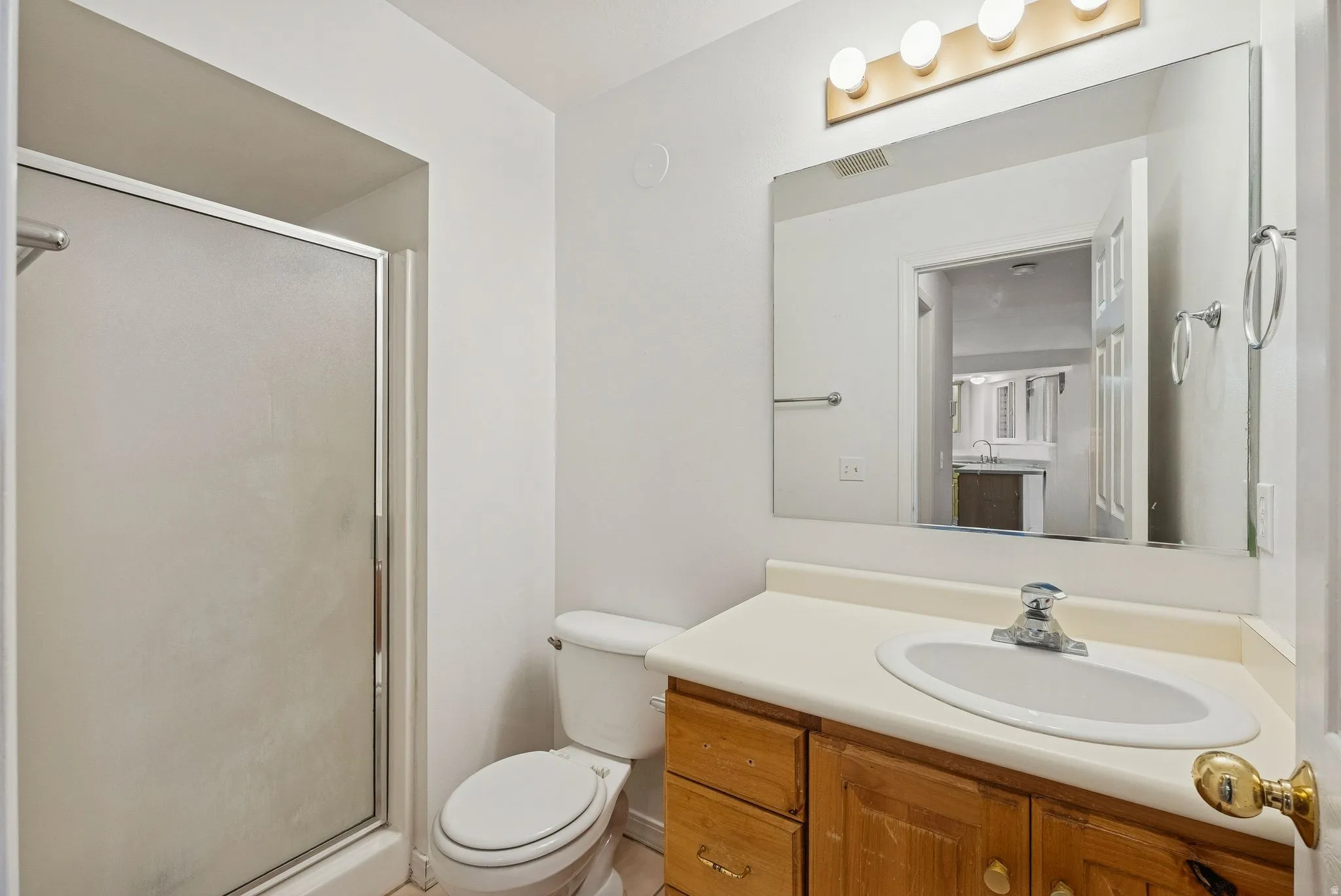 Bathroom featuring a walk-in shower with frosted glass enclosure, a vanity with wood-finish cabinetry, an integrated sink, a large wall-mounted mirror, and a three-bulb vanity light fixture