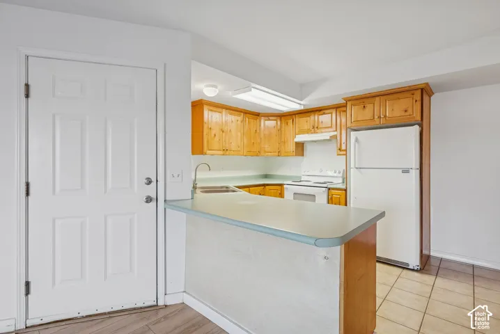 Kitchen featuring wood cabinetry, white appliances, light-toned countertops, and a breakfast bar