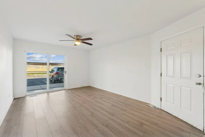 Spacious room featuring wood-finish flooring, a contemporary ceiling fan with integrated lighting, and a white paneled entry door