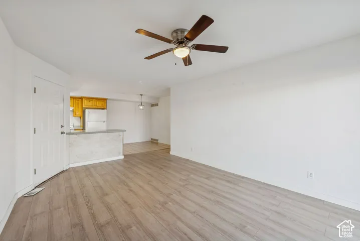 Open-concept living area featuring wood-finish flooring, a ceiling fan with integrated lighting, and a light-toned interior paint palette