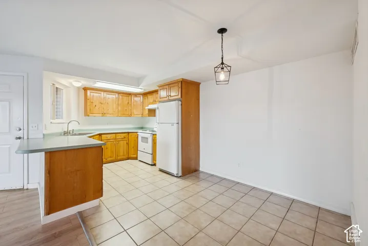 Kitchen and dining area featuring light wood cabinetry, white appliances, a peninsula with a countertop, tile flooring, and a contemporary hanging light fixture