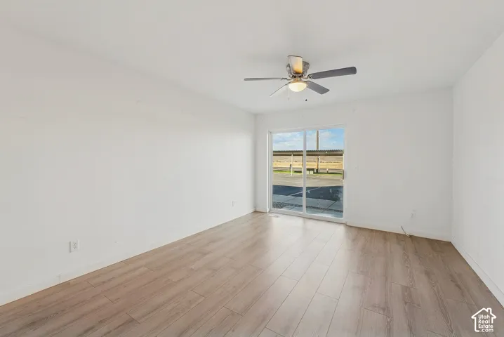 Spacious room featuring wood-finish flooring, white walls, and a ceiling fan with integrated lighting