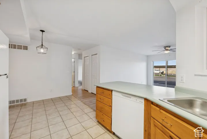 Kitchen area featuring light wood cabinetry, a built-in dishwasher, and a stainless steel sink with a light-colored countertop