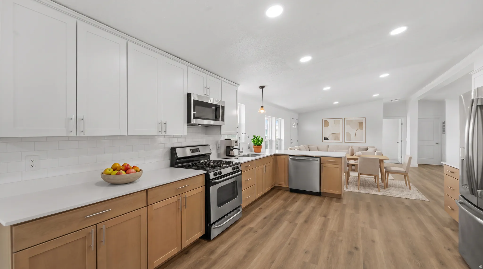 Open-concept kitchen featuring two-tone cabinetry, stainless steel appliances, white subway tile backsplash, and light wood-finish flooring