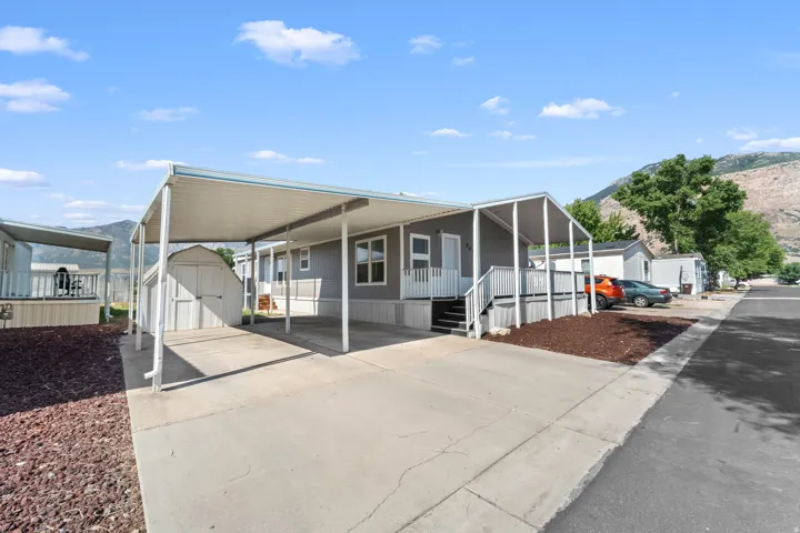 Gray exterior with white trim, featuring an attached carport, covered porch with white railing, and an exterior storage shed